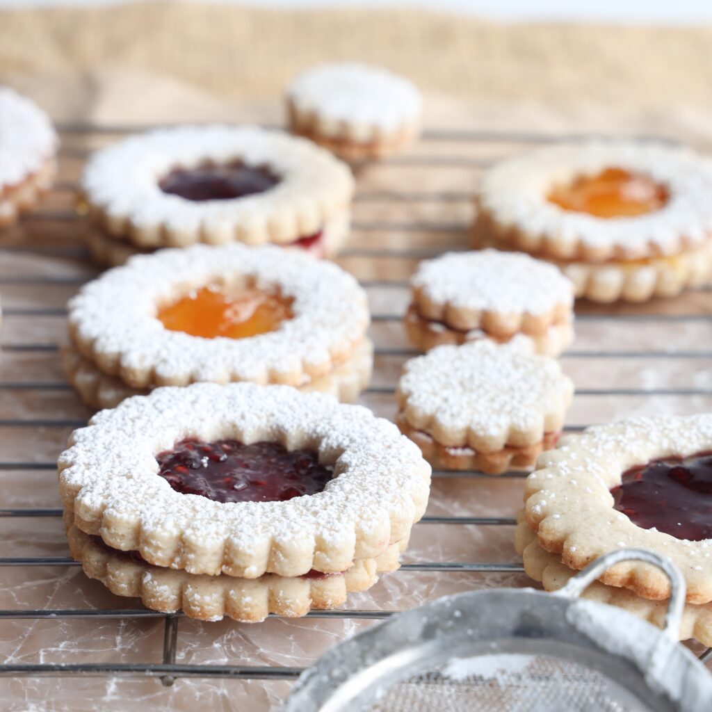 These gluten-free linzer cookies are easy to make, melt in your mouth, filled with raspberry and peach jam and the perfect gluten-free cookie for the holidays. A yummy shortbread like cookie with a jam filled centre that is almost too pretty to eat.