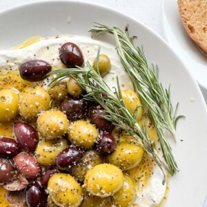 This olives and feta dip is ready in less than 15 minutes. Add olive oil, olives, dried oregano and rosemary to a frying pan and heat up. Add the hot olives to a whipped feta and serve. An easy to make, delicious gluten-free appetizer for the holiday season that friends and family will enjoy.